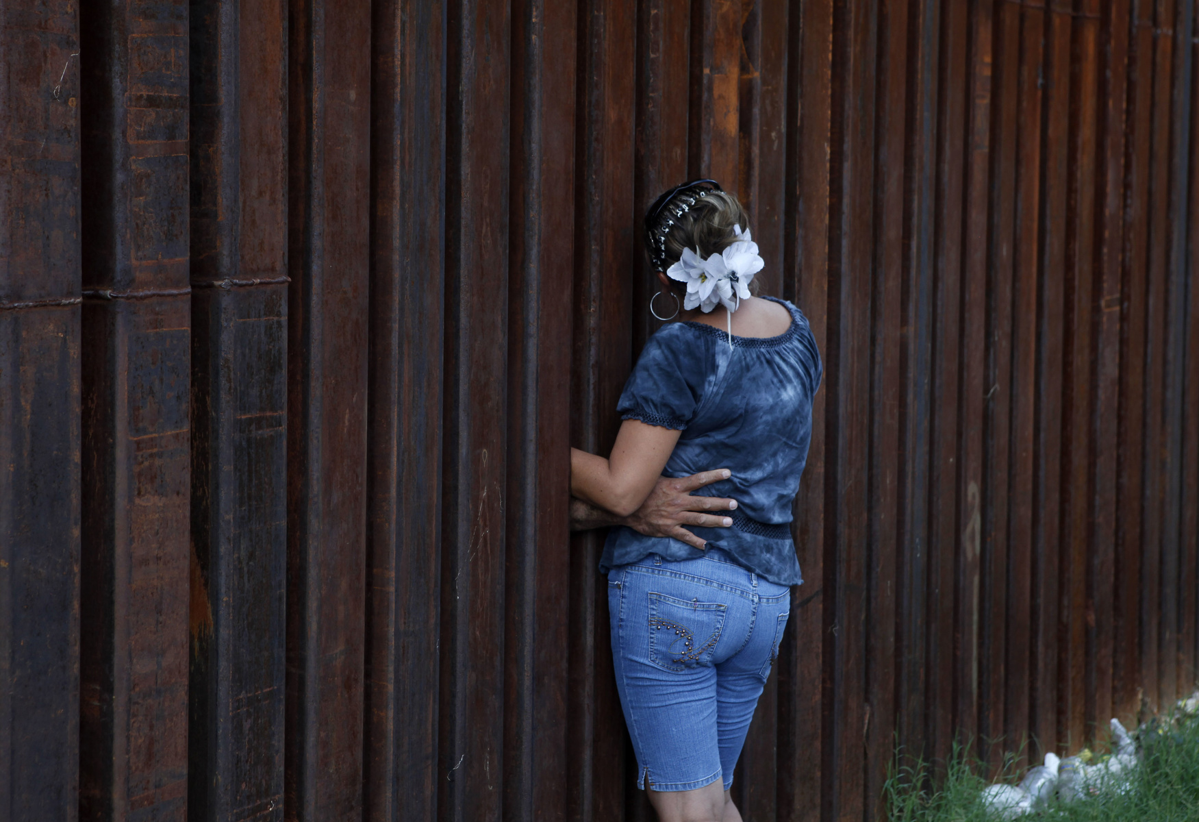 A woman, who declined to give her name, is hugged by her husband as they chat between the border fence separating Nogales, Ariz., and Nogales, Sonora, Mexico, Wednesday, July 28, 2010. A federal judge on Wednesday blocked the most controversial parts of Arizona's immigration law from taking effect, delivering a last-minute victory to opponents of the crackdown. The overall law will still take effect Thursday, but without the provisions that angered opponents — including sections that required officers to check a person's immigration status while enforcing other laws. (AP Photo/Jae C. Hong)